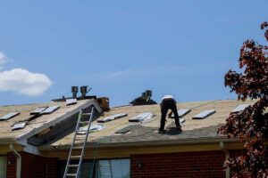 Person inspecting damaged shingles and water stains on a house roof with visible wear and missing sections.