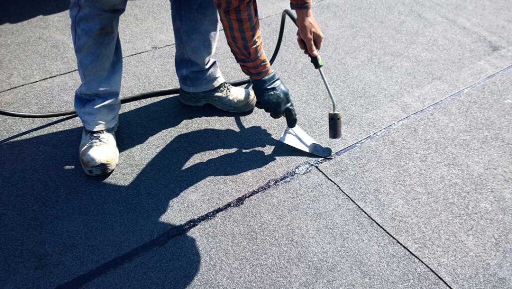 A homeowner examines roof shingles for damage from a ladder during spring.