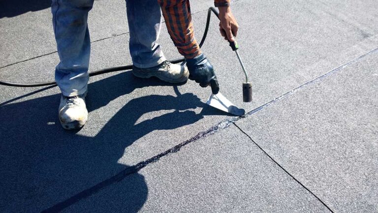 A homeowner examines roof shingles for damage from a ladder during spring.