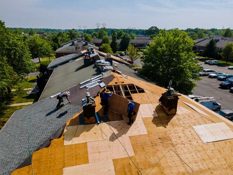 Roofing workers examine modern shingles, synthetic underlayment, flashing, and solar roofing components on a winter-ready home.